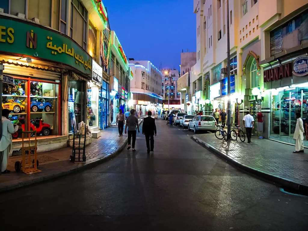 Shops with Arabic and English name boards along a street in old Deira at dusk