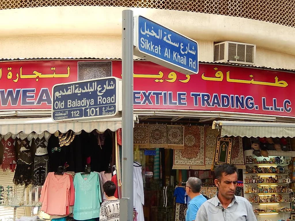 A bilingual Arabic and English shop sign ending in Textile Trading L.L.C. above a Dubai souk shop