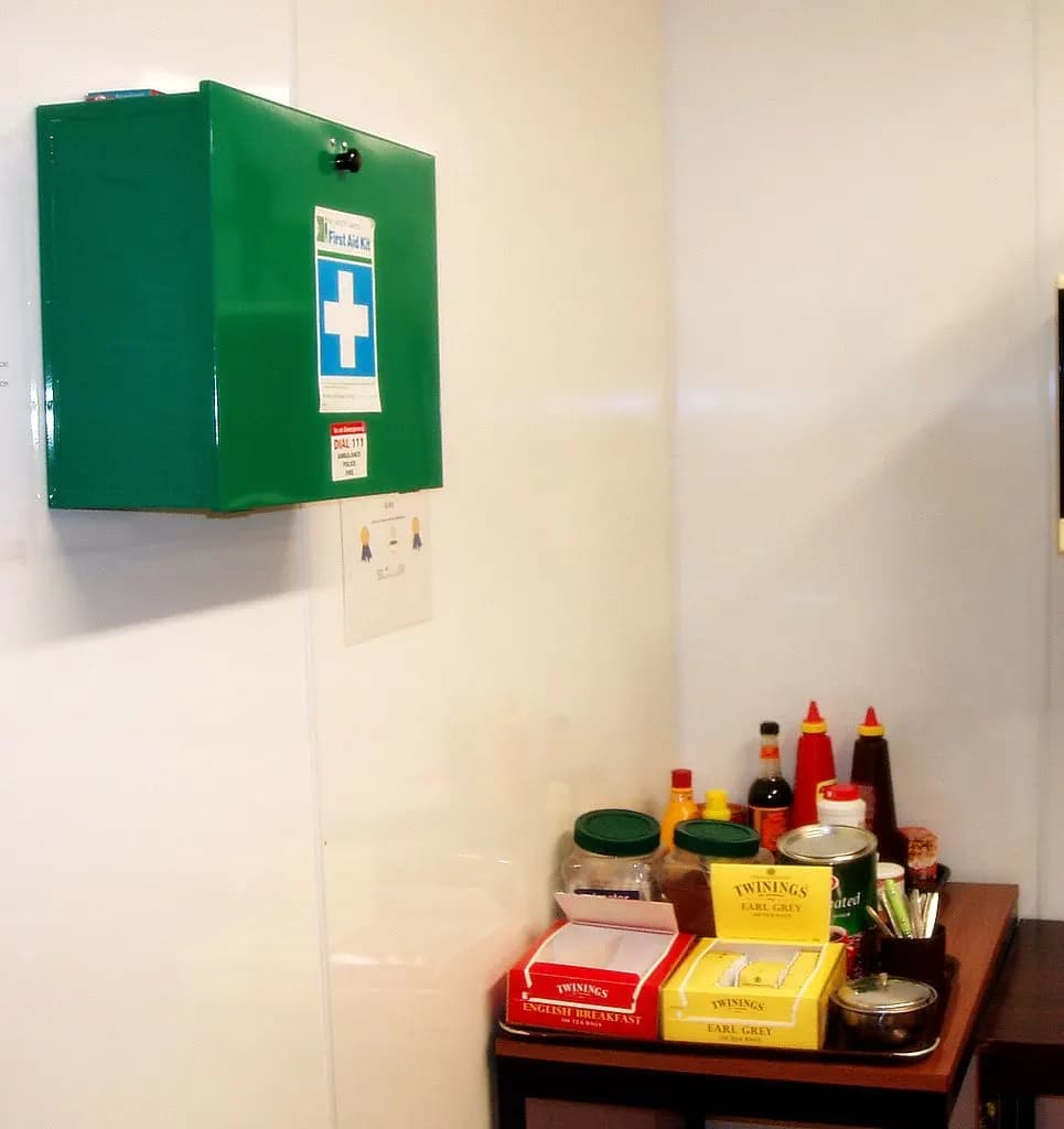 A green first aid kit mounted on a white wall in a staff kitchen