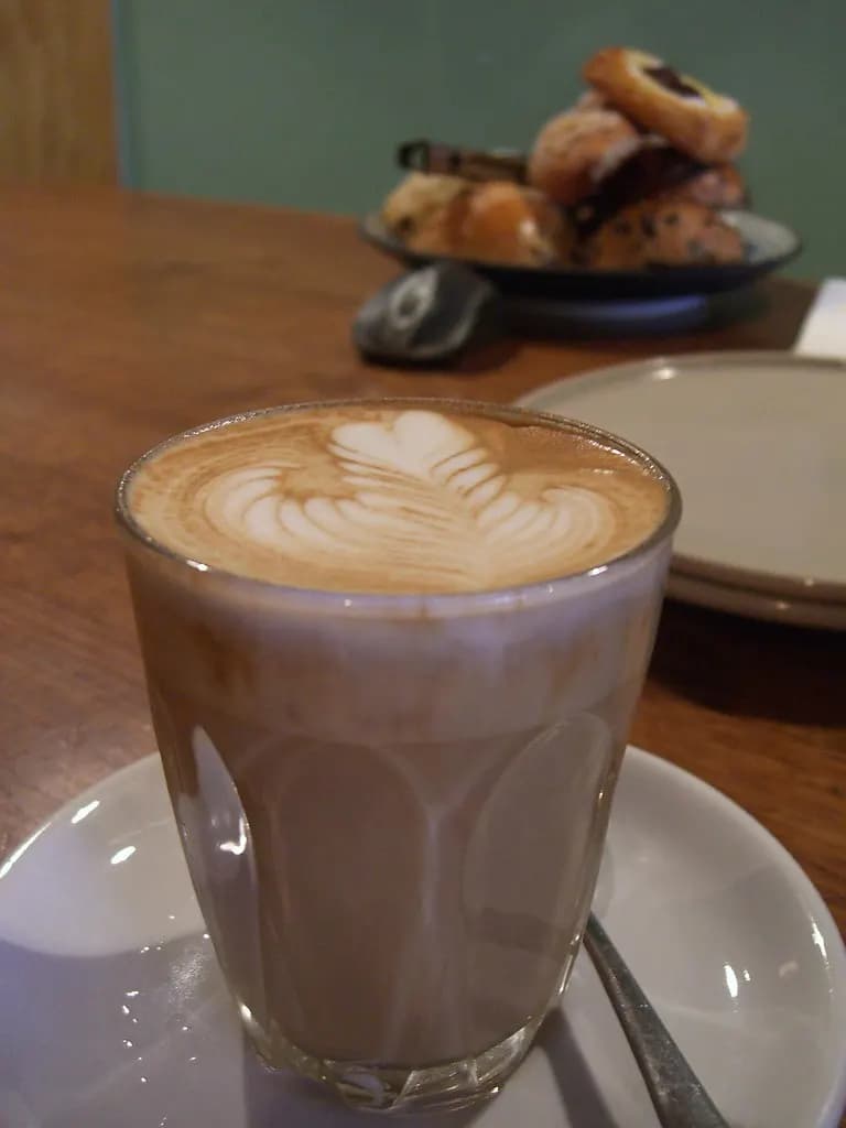 A caffe latte with latte art in a glass on a cafe table, with pastries in the background