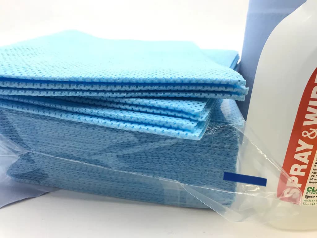Blue and white cleaning cloths beside an antibacterial spray bottle