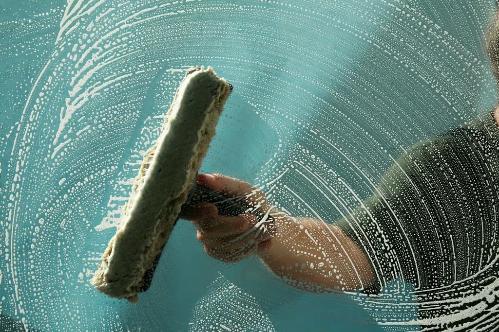 A window cleaner soaping a large glass window with a washing wand before squeegeeing it