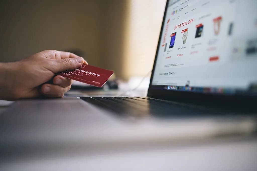 A shopper holding a bank card next to a laptop showing an online store's product page