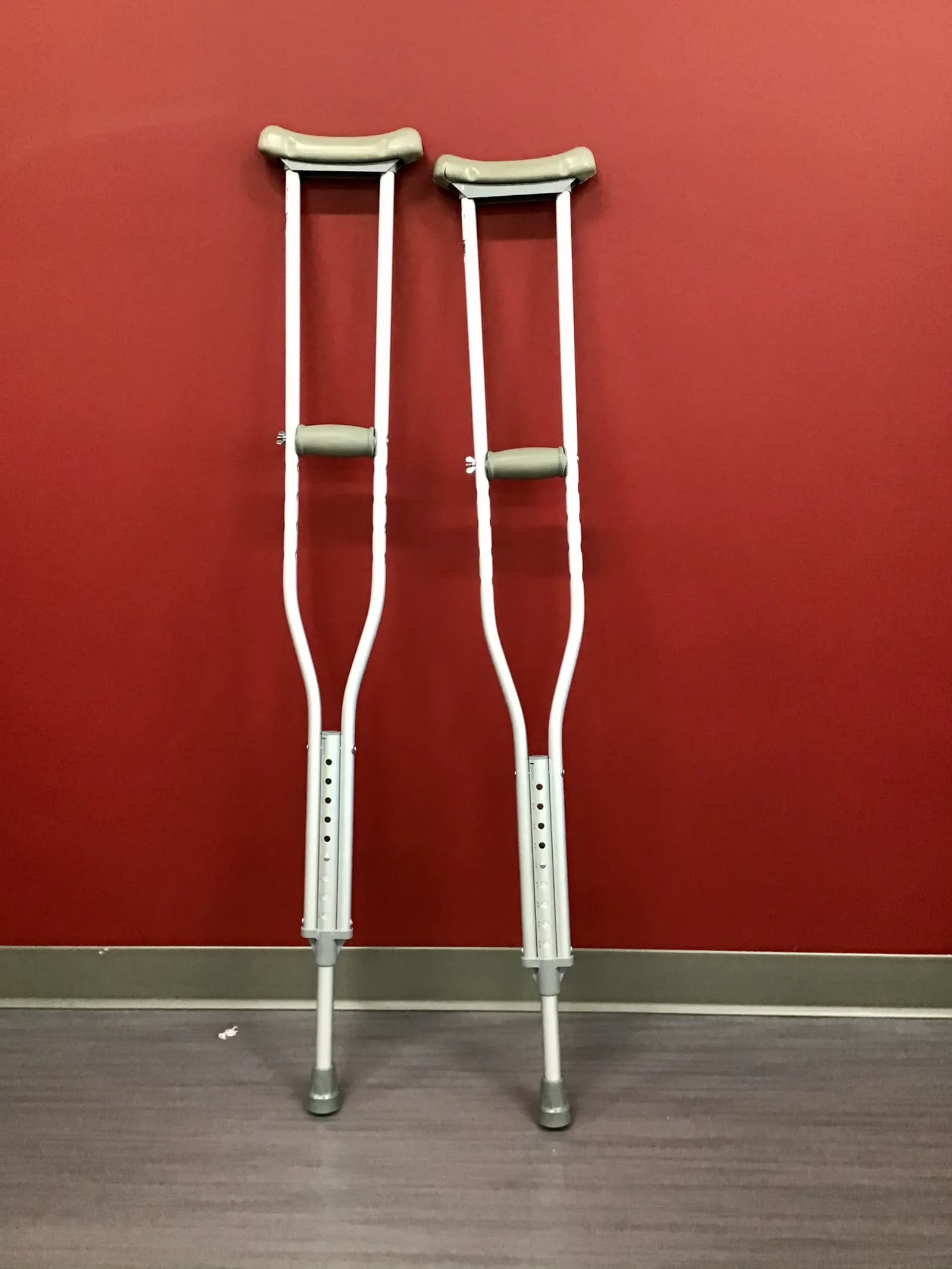 A pair of adjustable aluminium underarm crutches leaning against a red wall