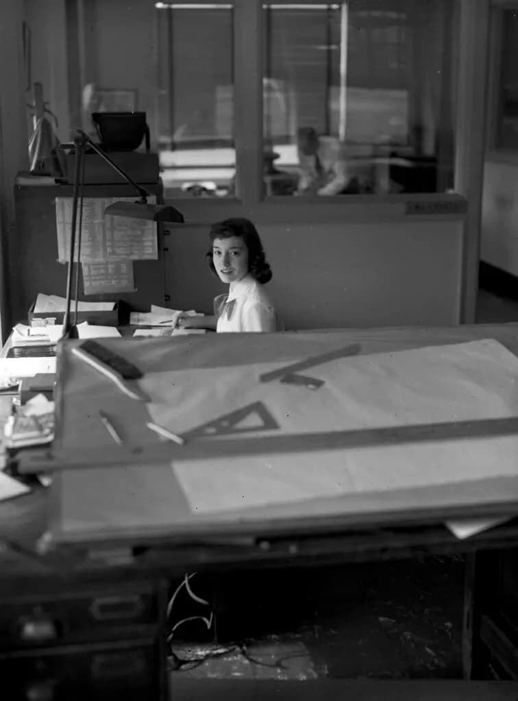 Clerk at a desk in a 1950s company office, with a drafting table in the foreground