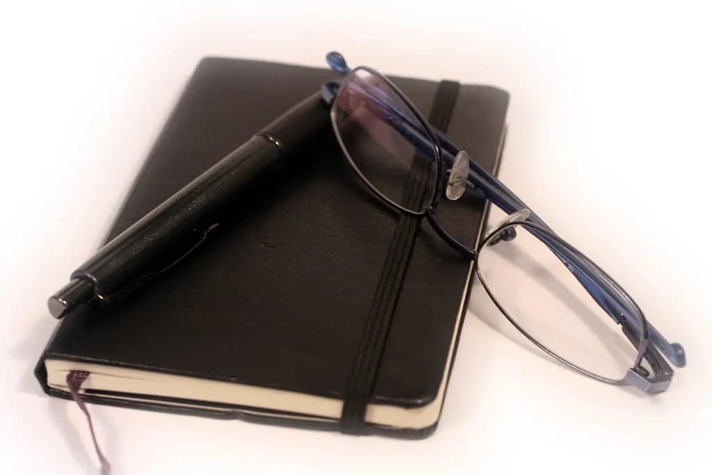 A black diary with a pen and reading glasses resting on it