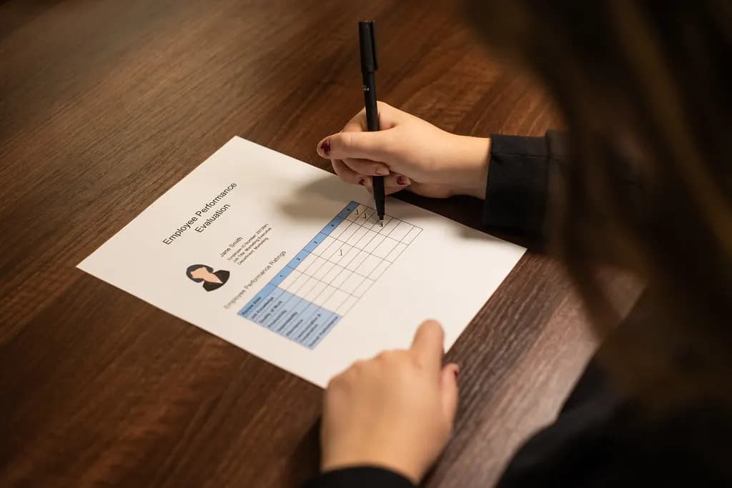 An employee performance review form on a wooden desk with a hand holding a pen