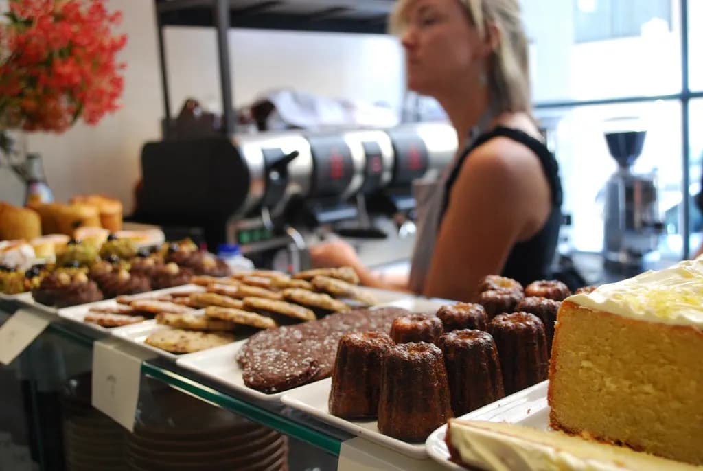 Café counter in Melbourne with cakes and pastries in front and a staff member working at the espresso machine