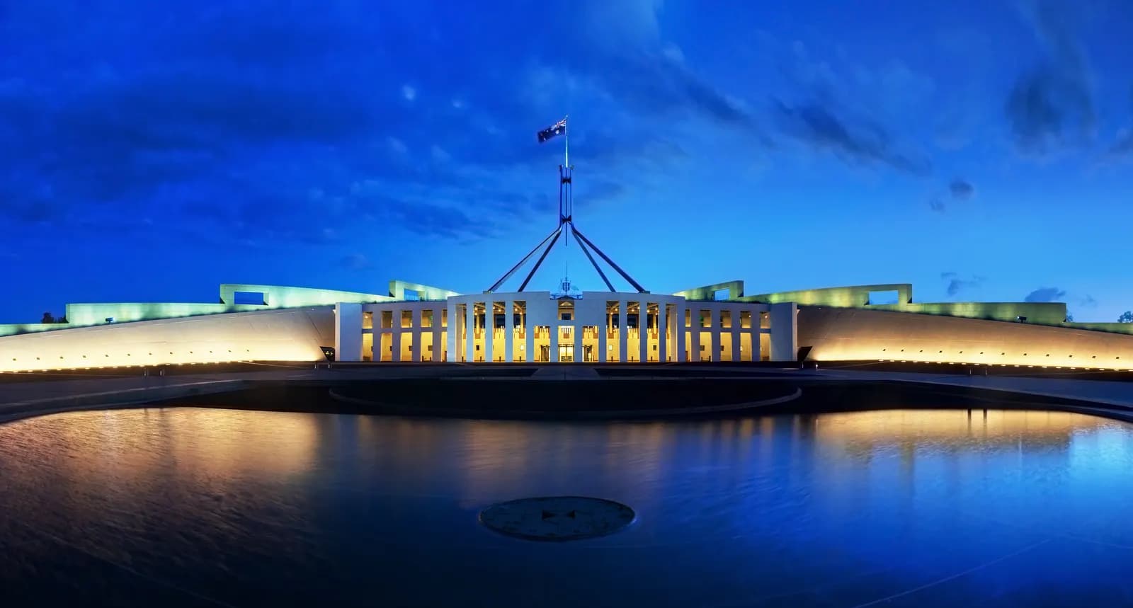 Parliament House in Canberra at dusk with its flagpole lit above the building