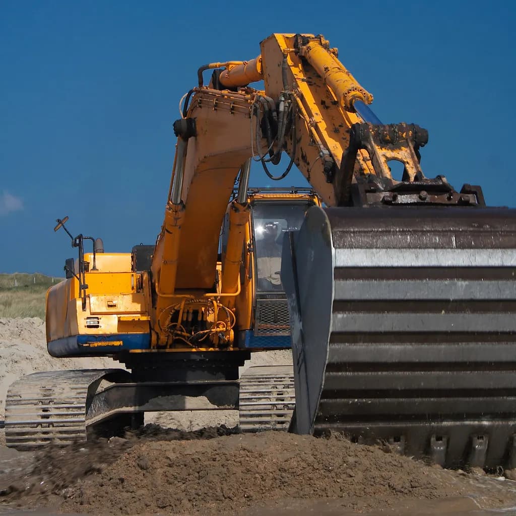 Yellow tracked excavator with a large bucket on a mound of earth at a work site
