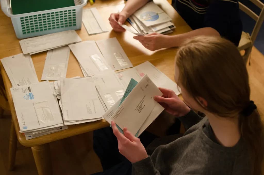 Two people sorting a table covered in opened envelopes and paper statements