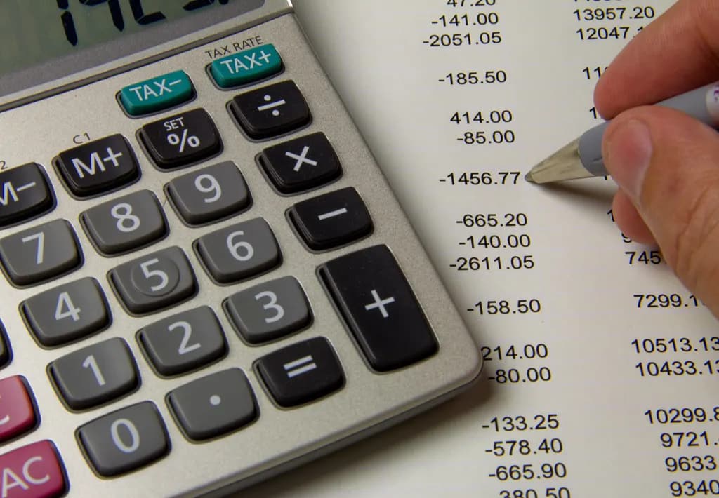 Calculator beside a printed statement while a hand checks figures with a pen