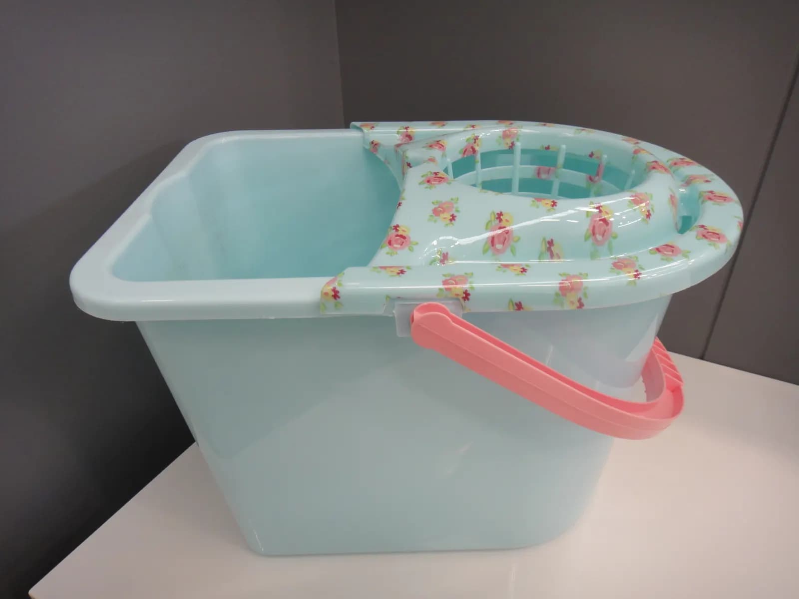 A plastic mop bucket with a built-in wringer on a white floor