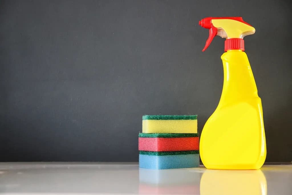 An unlabelled yellow spray bottle beside a stack of three scrub sponges