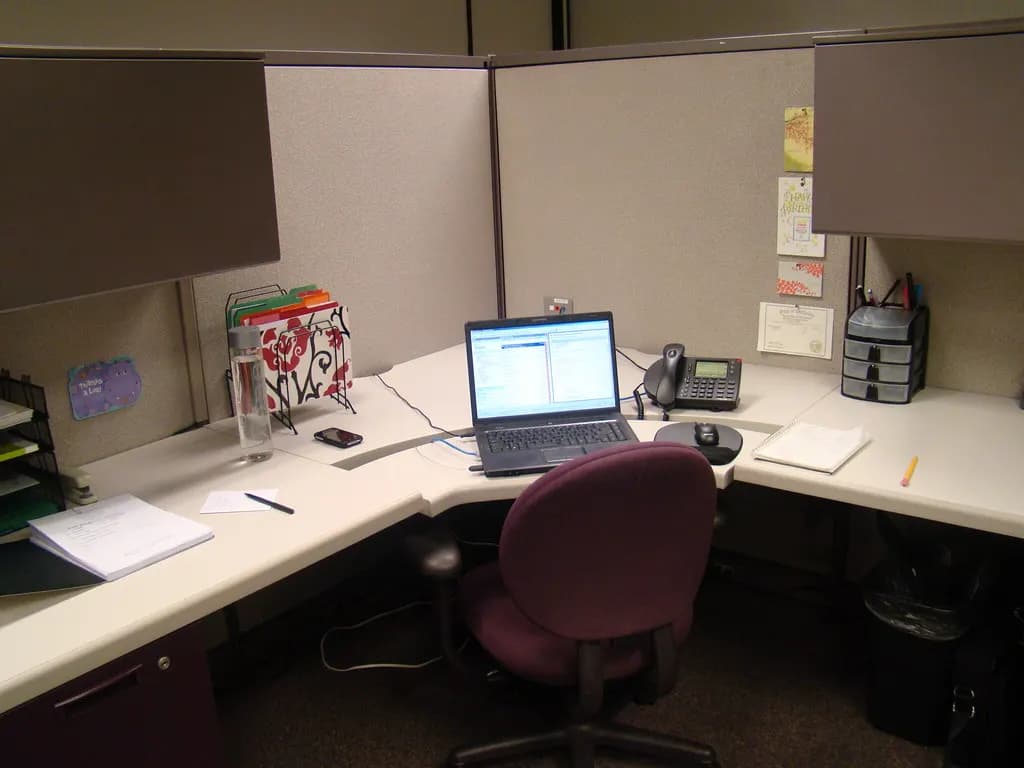 An empty office cubicle with a laptop open on the desk and an office chair