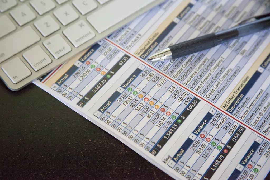 A printed payroll spreadsheet with a pen resting on it beside a computer keyboard