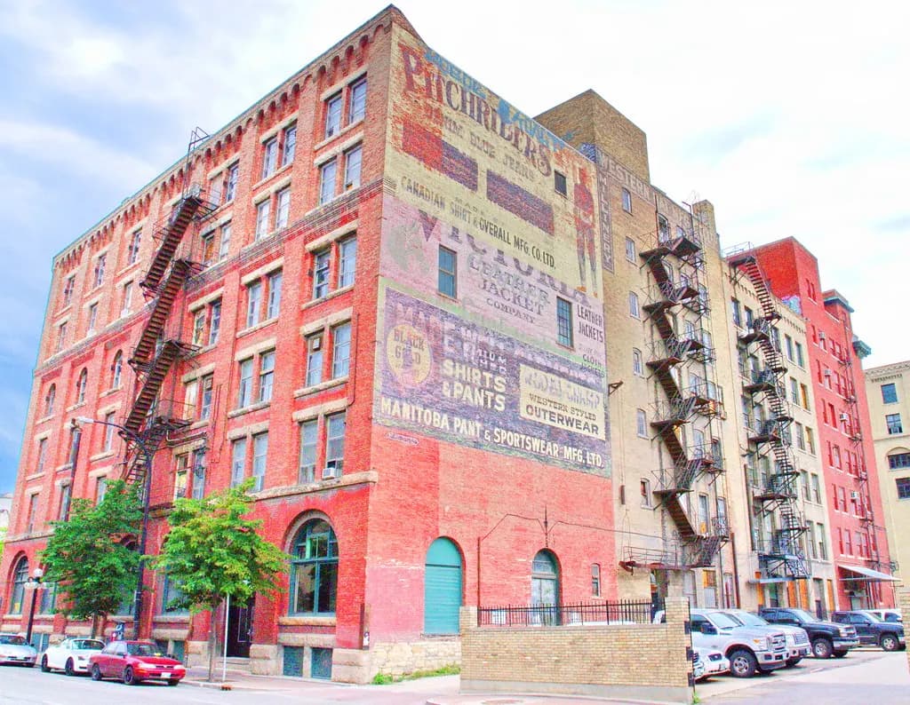 Red-brick warehouse in Winnipeg's Exchange District with faded painted business signs and fire escapes