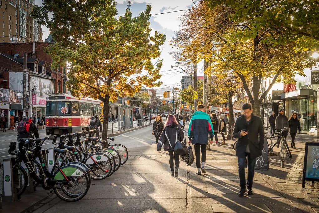 Shoppers walking past storefronts and a streetcar on Queen Street West in Toronto in autumn