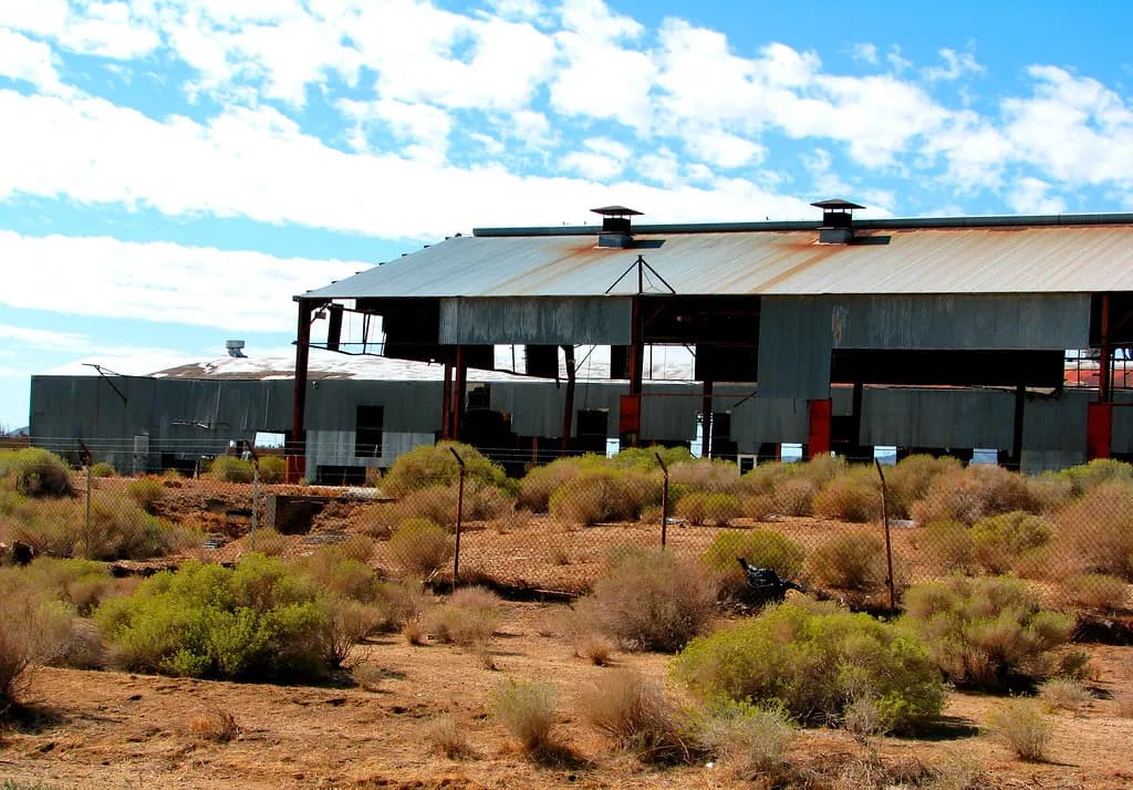 A disused industrial shed with corrugated metal walls behind an overgrown lot