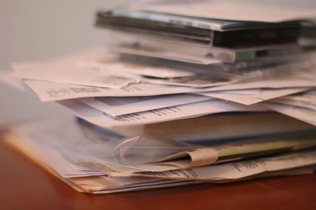 A loose pile of paper forms and receipts on a wooden desk