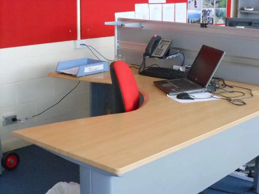 An empty office desk with a laptop, desk phone and a red chair
