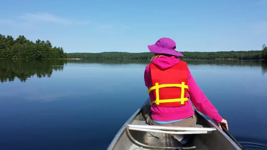 A person in a life jacket paddling a canoe on a calm lake in Bon Echo Provincial Park, Ontario