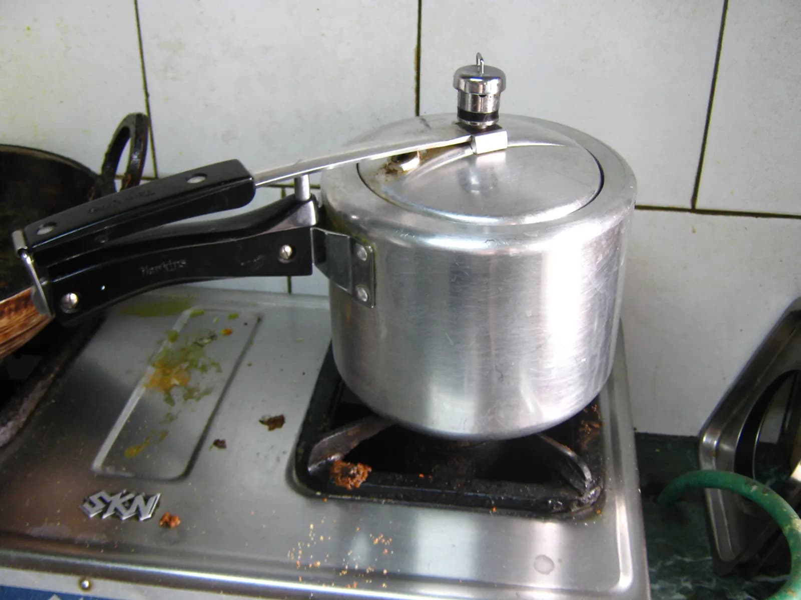 An aluminium pressure cooker sitting on a gas stove in an Indian home kitchen