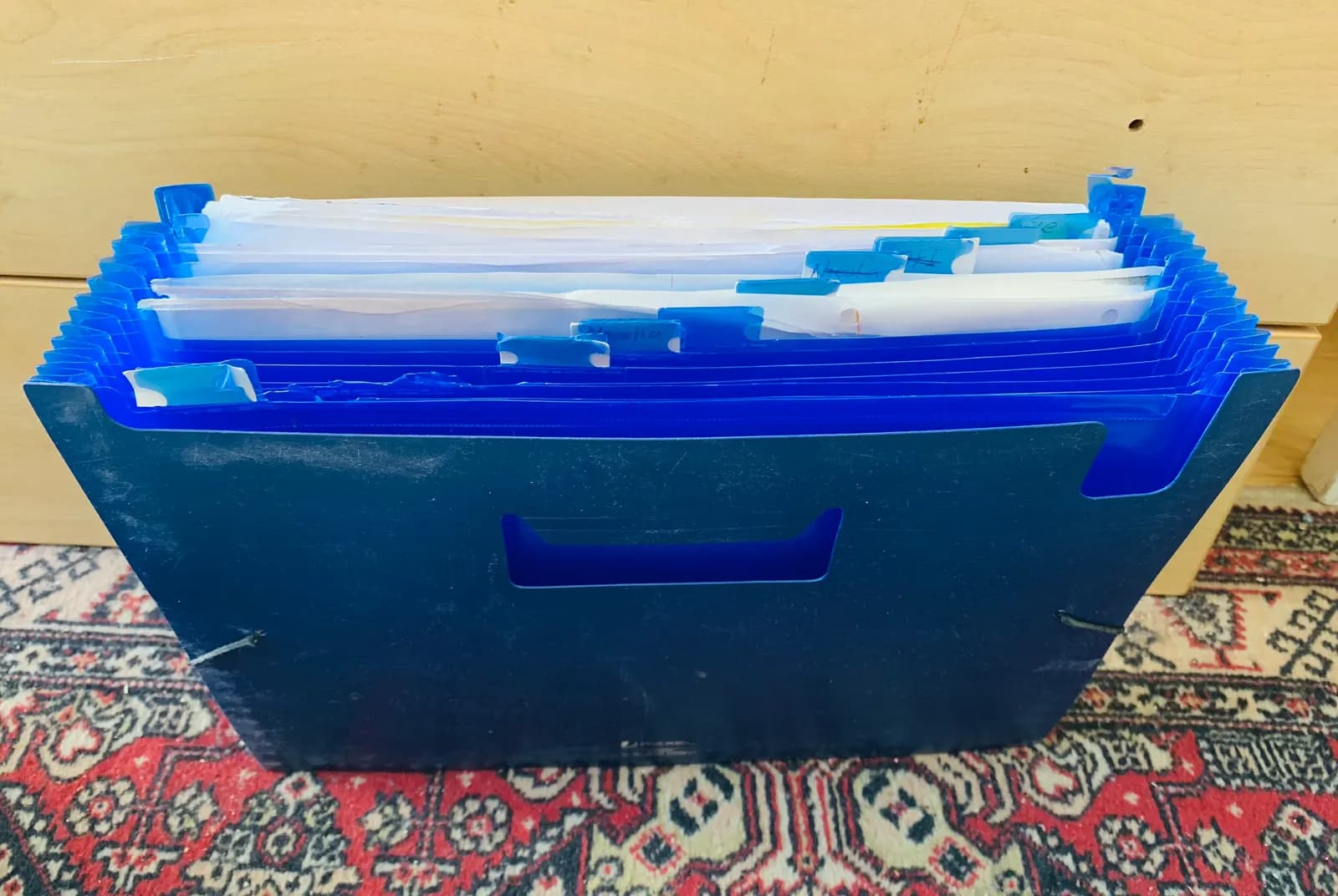 A blue accordion file folder with labelled tabs, packed with papers