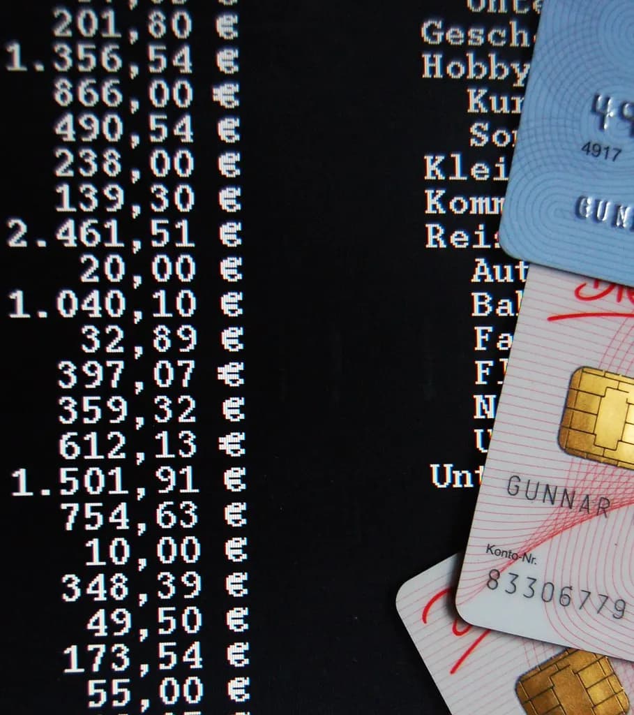 Close-up of a printed bank account statement listing transaction amounts, with bank cards on top
