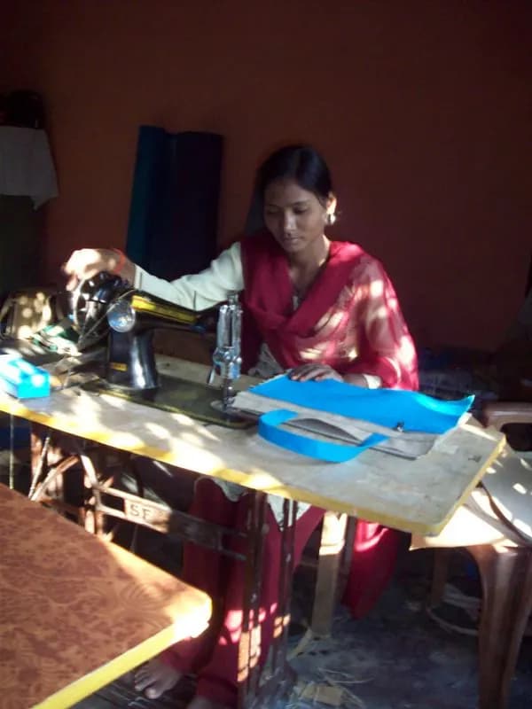 A woman stitching blue fabric on a treadle sewing machine in a small tailoring room in a village near Lucknow