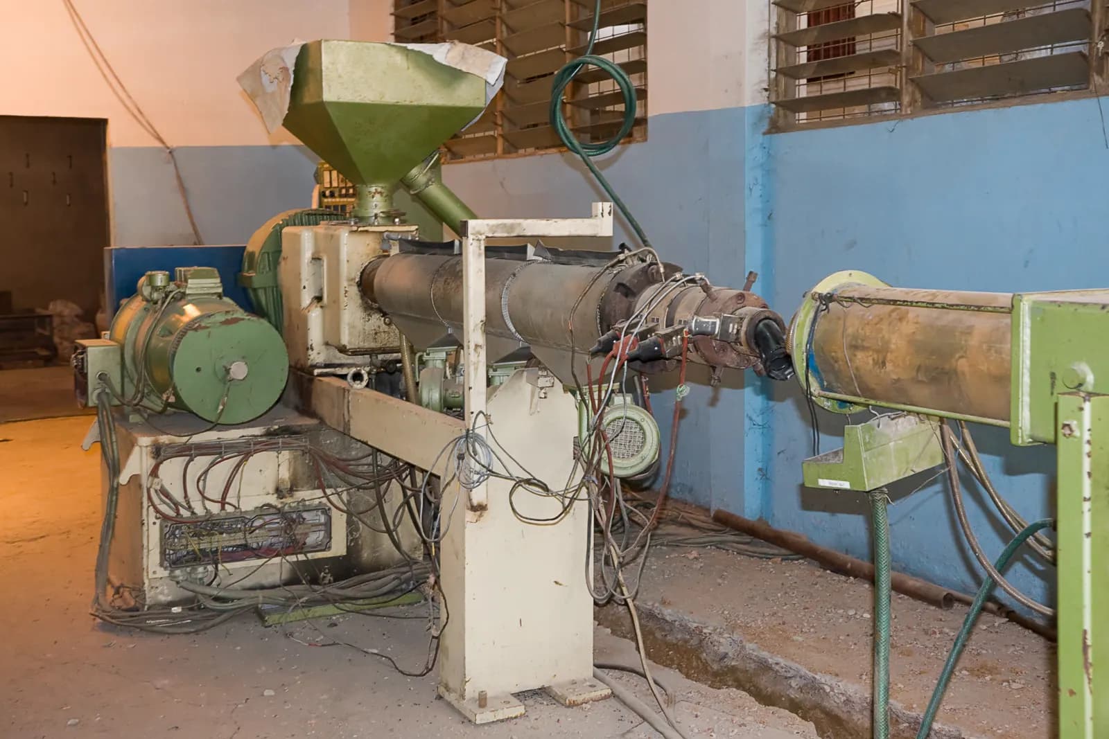 A single-screw plastics extruder with its feed hopper, heated barrel and die on a factory floor