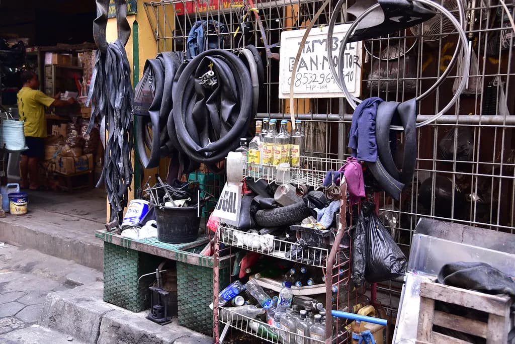 A small tyre and tube repair shop on a market back street in India, with tubes hanging on racks