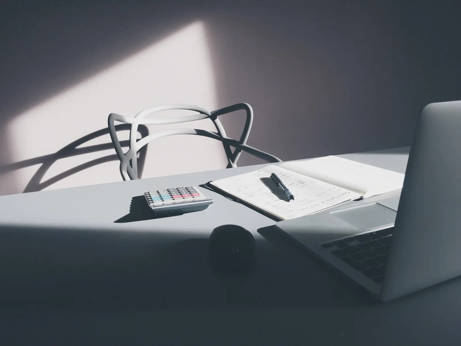 Desk with a calculator, an open notebook with handwritten figures, a pen and a laptop