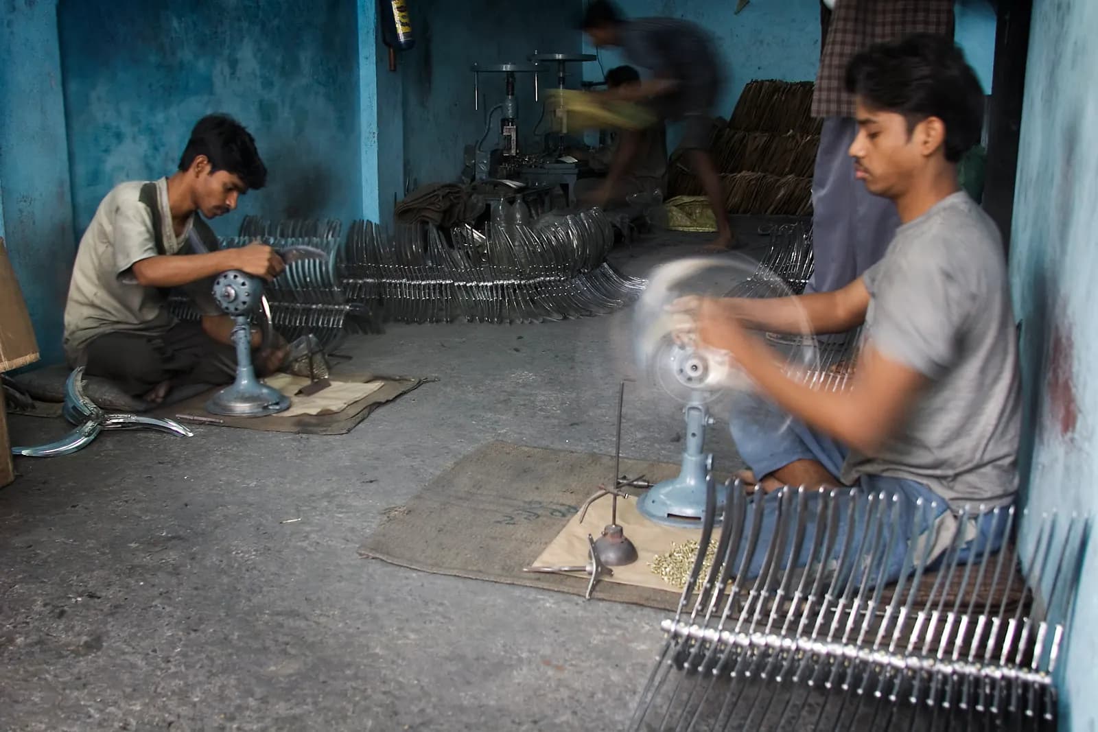 Two workers assembling electric table fans on the floor of a small factory in Varanasi