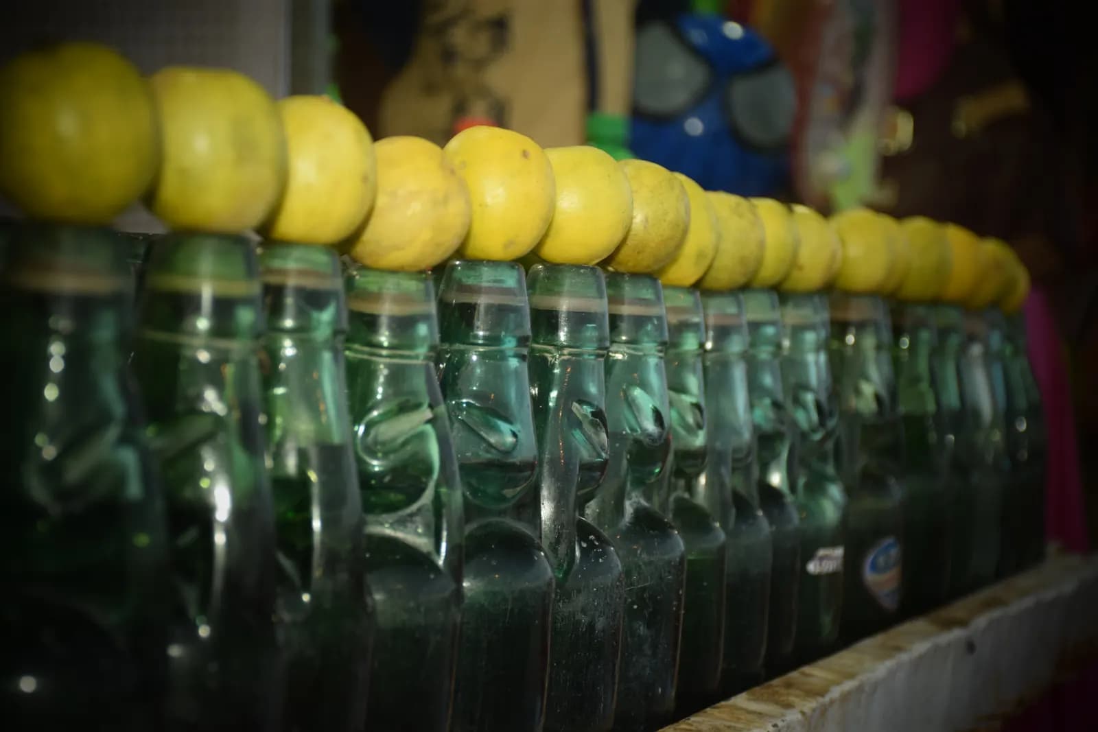 A row of green goli soda bottles, each topped with a lemon, at a street stall