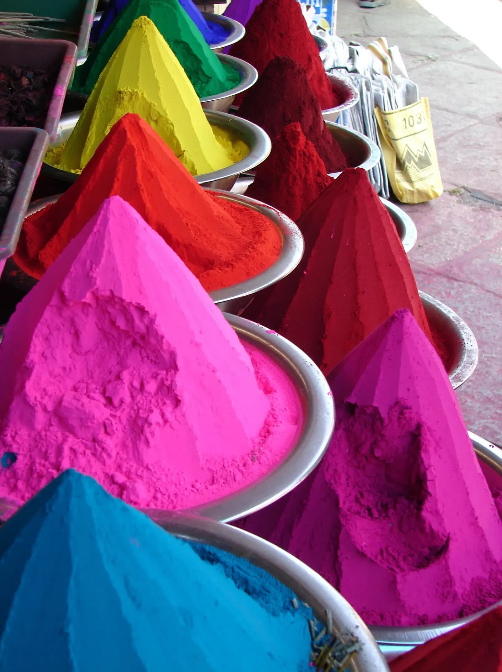 Cones of kumkum and coloured powders in pink, red, yellow, green and blue heaped in steel bowls at a market stall