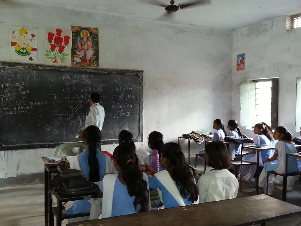 A teacher explains a maths lesson on a blackboard to a class of secondary school girls in India