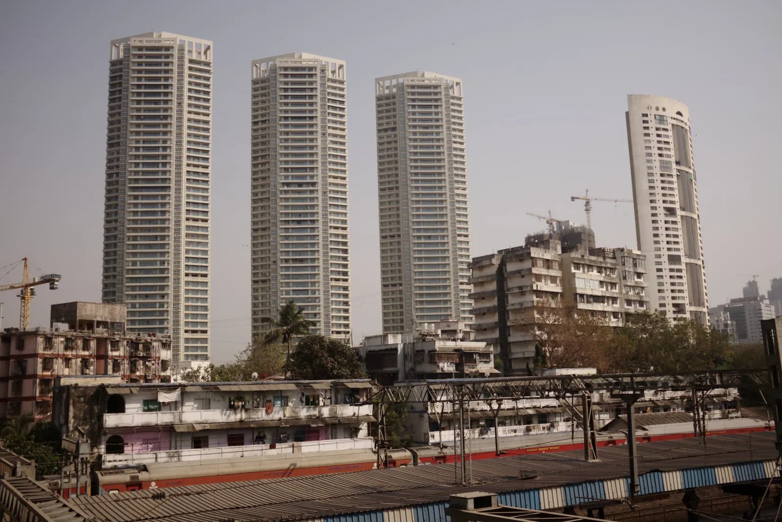 Completed high-rise residential towers beside older apartment blocks and a railway line in Mumbai