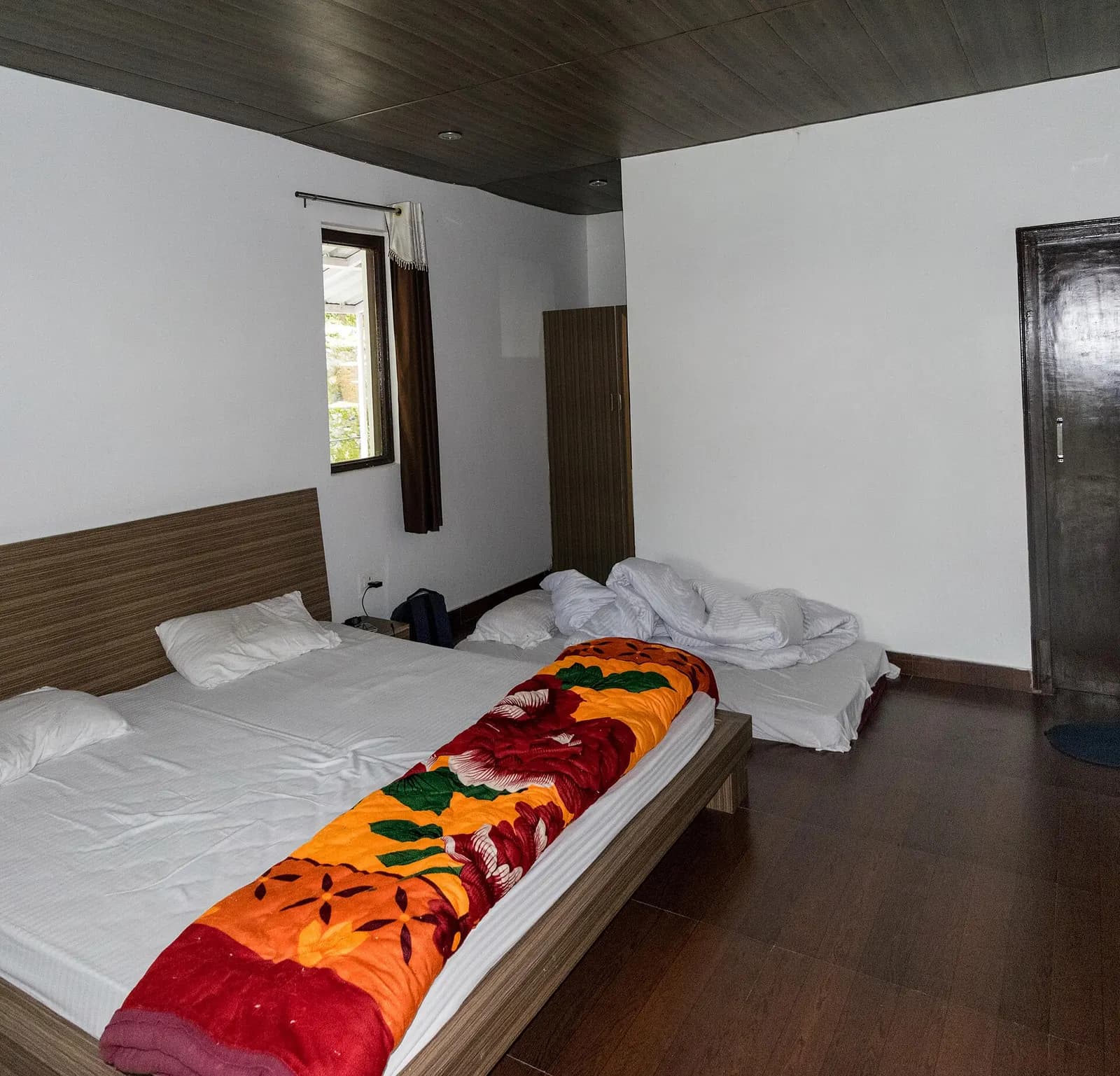 A simple hotel room with a double bed, wooden headboard, white walls and a window