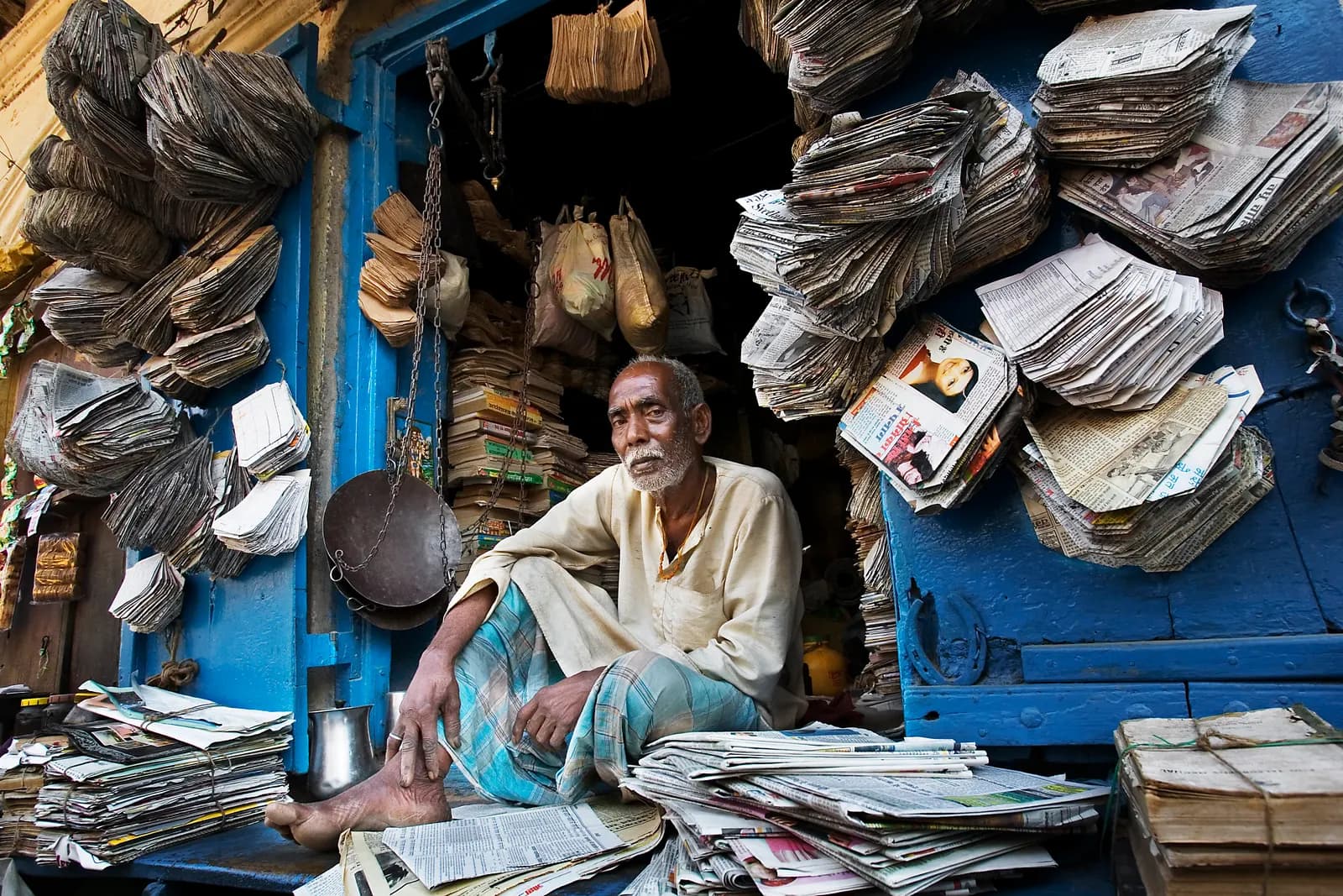 Paper bag maker in Varanasi seated in his shop surrounded by bundles of bags made from old newspaper