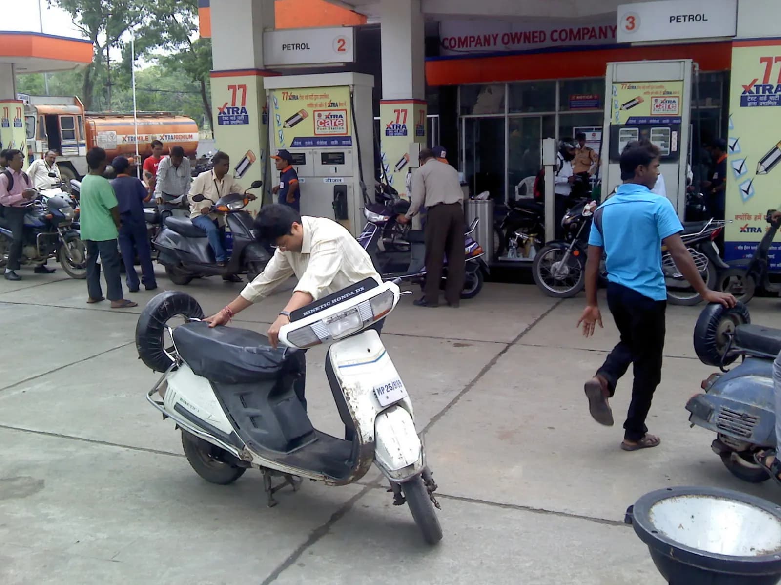 Scooter and motorcycle riders refuelling at a busy petrol pump forecourt in Nagpur