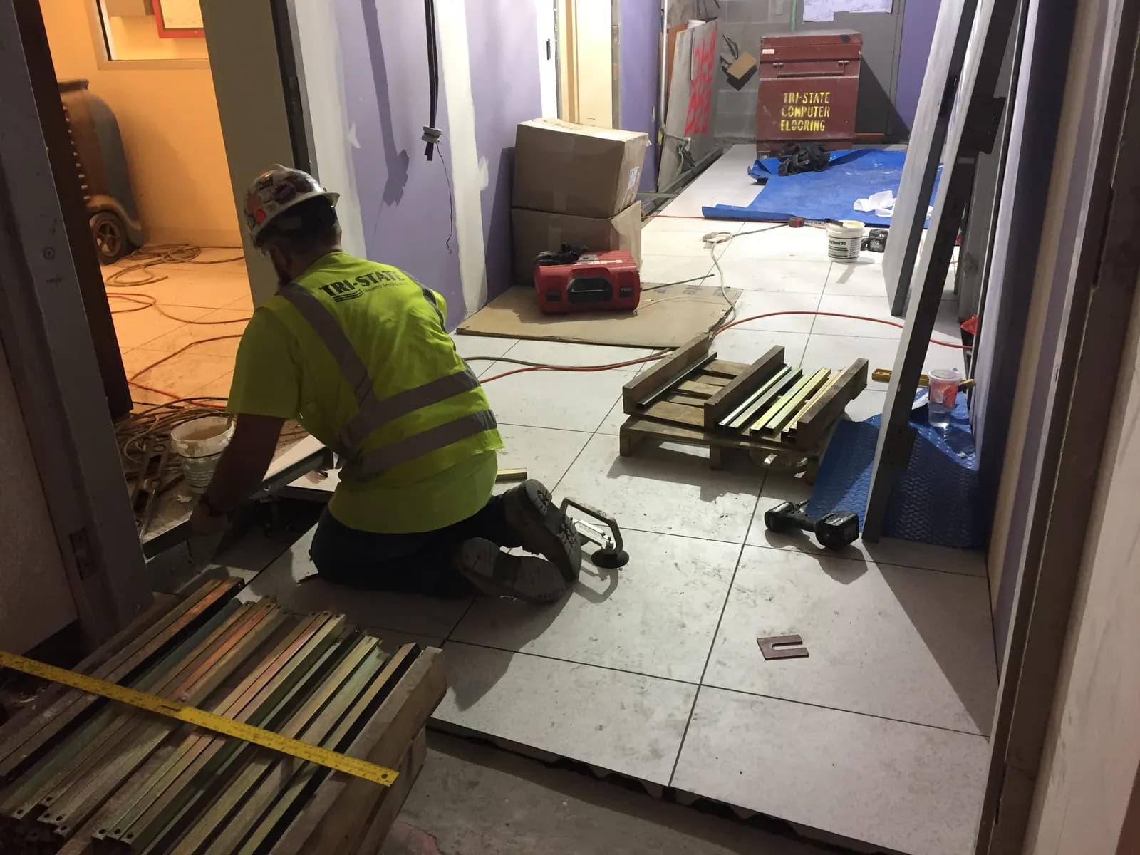 A worker kneeling to lay large-format floor tiles in a building under construction