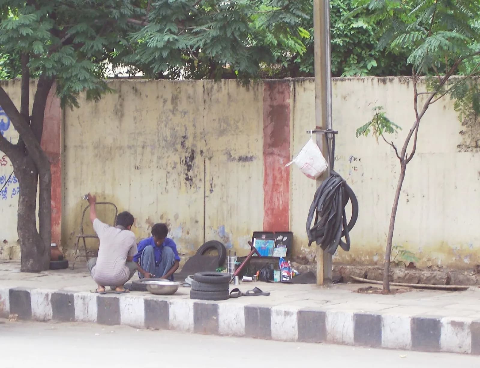 Two men repairing tyres and inner tubes at a roadside stall on a Hyderabad pavement