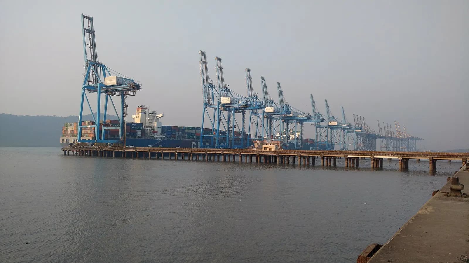 Ship-to-shore container cranes lined up along the berth at Jawaharlal Nehru Port, Navi Mumbai, with a container ship alongside
