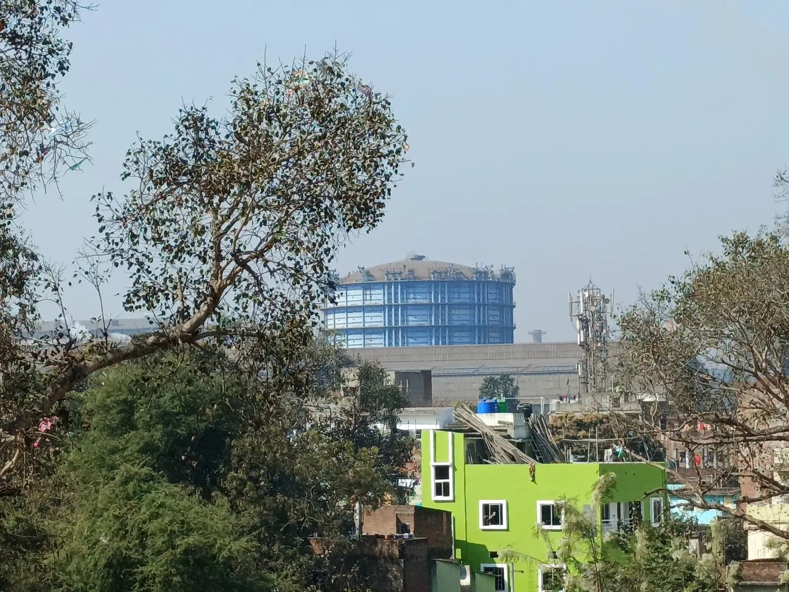 View across trees and houses in Jamshedpur towards a large blue gas holder at the Tata Steel works