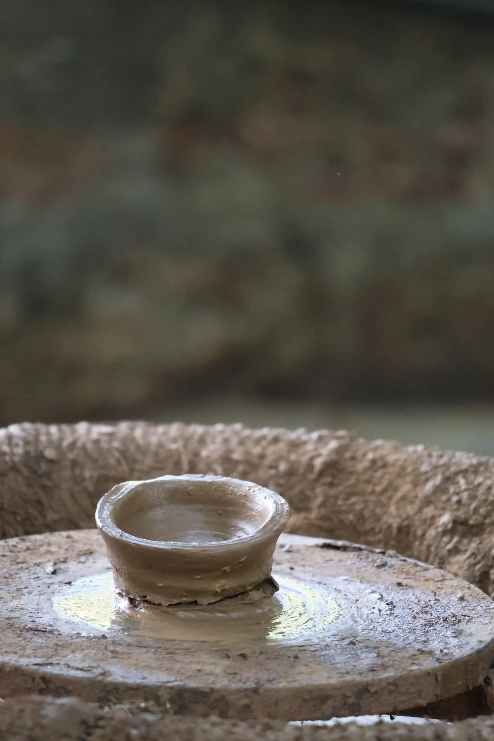 A small clay pot being shaped by hand on a traditional potter's wheel in India
