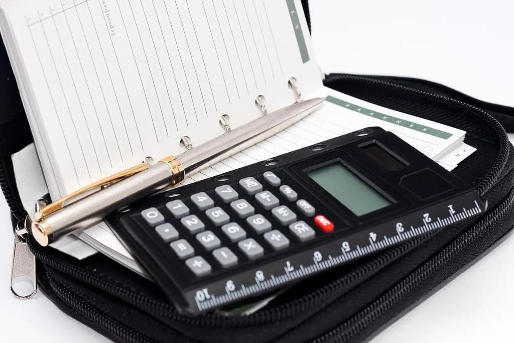 A calculator, pen and notepad in an open organiser case