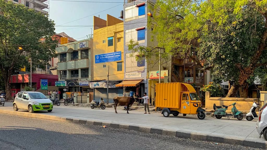 A Bengaluru street with small shops, a delivery van and scooters parked outside