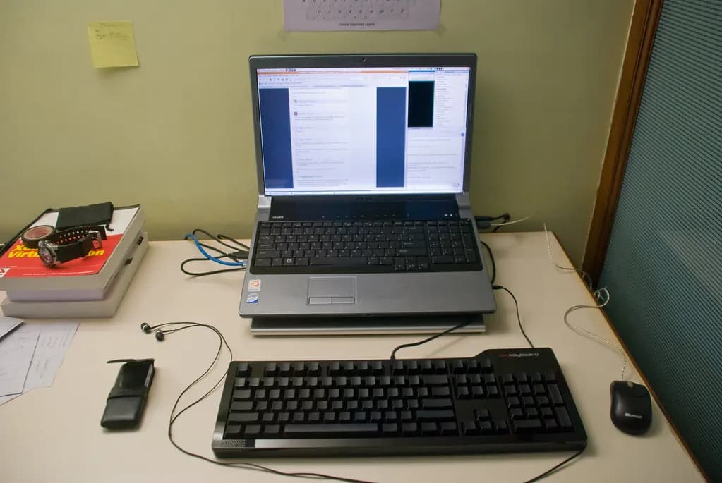 A small office desk with a laptop, keyboard, mouse and notebooks