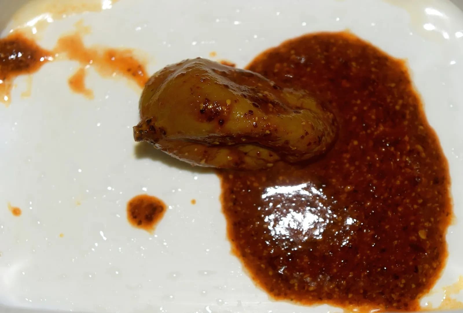 A piece of tender mango pickle in thick red chilli-mustard masala on a white plate